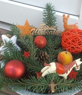 weihnachtliches Gesteck aus Tanne mit ruten Kugeln, Sternen, Äpfeln, Rehlein, Tannenzapfen, Pferd und dem Schriftzug: "Frohe Weihnachten"