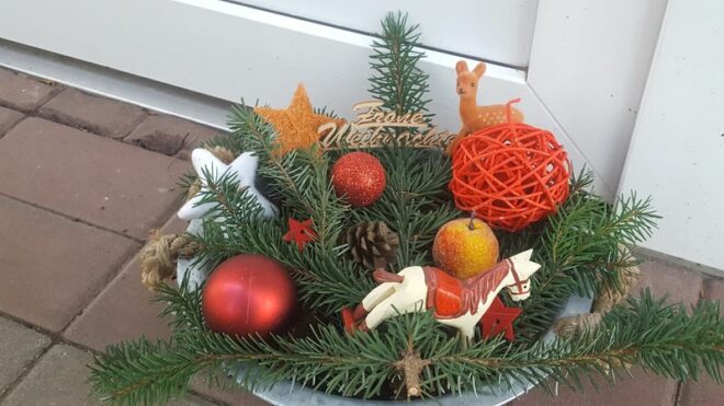weihnachtliches Gesteck aus Tanne mit ruten Kugeln, Sternen, Äpfeln, Rehlein, Tannenzapfen, Pferd und dem Schriftzug: "Frohe Weihnachten"